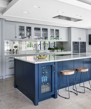 Kitchen with mirror tiled wall, white walls, and dark blue kitchen island with bar stools.
