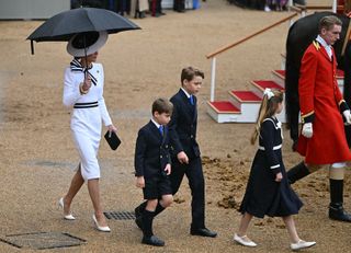 Catherine, Princess of Wales, shelters from the rain with an umbrella as she walks with her children Britain's Prince George of Wales (C), Britain's Princess Charlotte of Wales (R) and Britain's Prince Louis of Wales back to the Glass State Coach at Horse Guards Parade during the King's Birthday Parade "Trooping the Colour" in London on June 15, 2024.