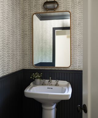 powder room with gray wallpaper, black panelling, basin, brass mirror and wall light