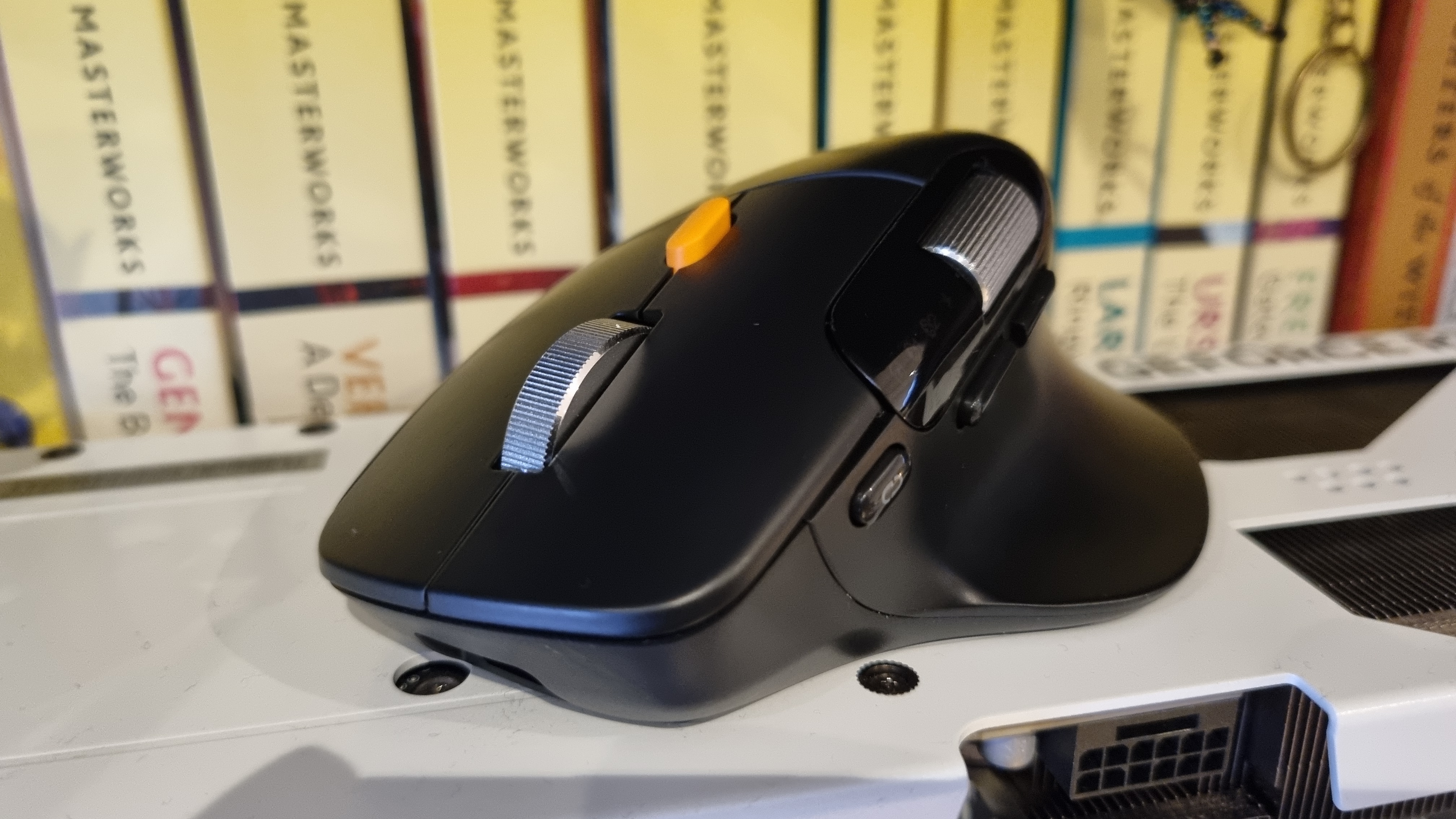 A ProtoArc EM25 ergonomic mouse on top of a graphics card, in front of various sci-fi novels