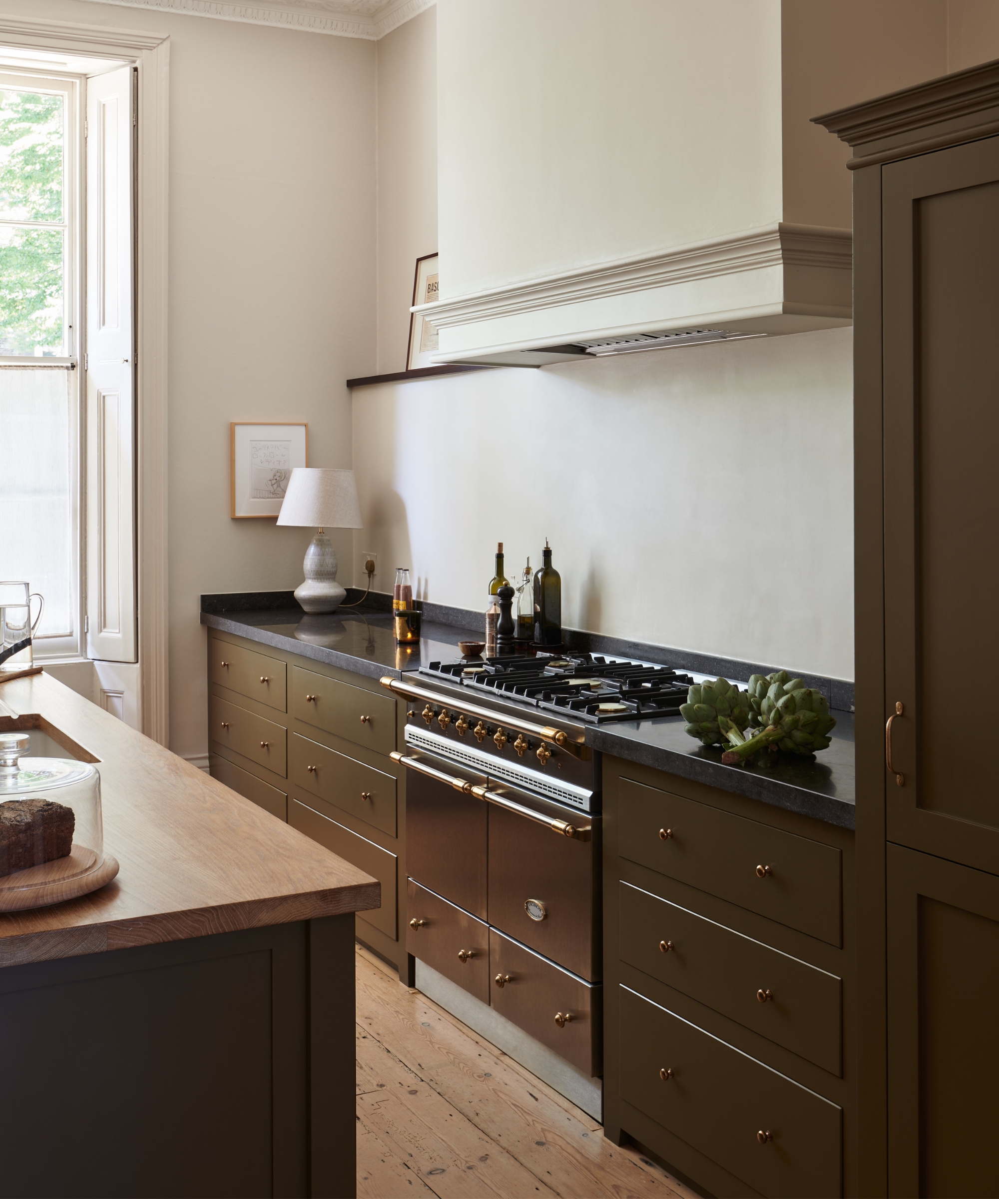 A classic kitchen with white walls, olive green cabinets, and brass hardware