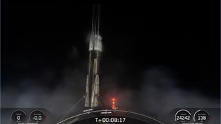 A black and white spacex falcon 9 rocket first stage sits on the deck of a ship at sea at night