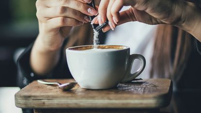 how to sweeten coffee without sugar: sugar being poured into coffee on a wooden table