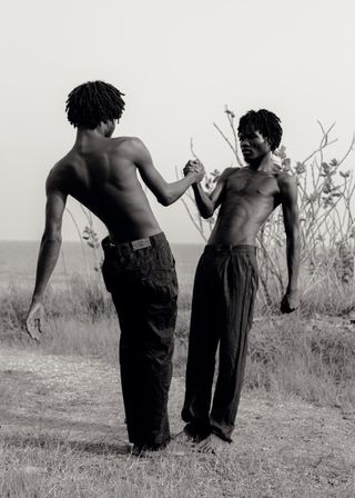 Two African men wearing no shirts and jeans shaking hands.