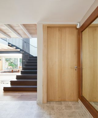 Light oak slab door next to a modern open staircase and mirrored wall