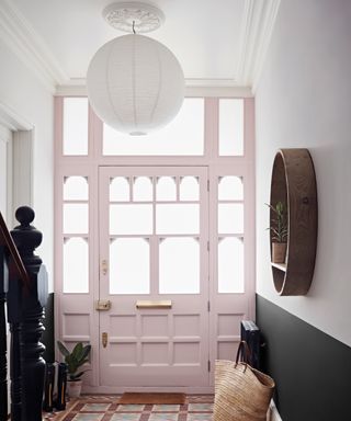 Glass paneled front door with light pink painted contrast, in in bright hallway, with two tone mono wall.