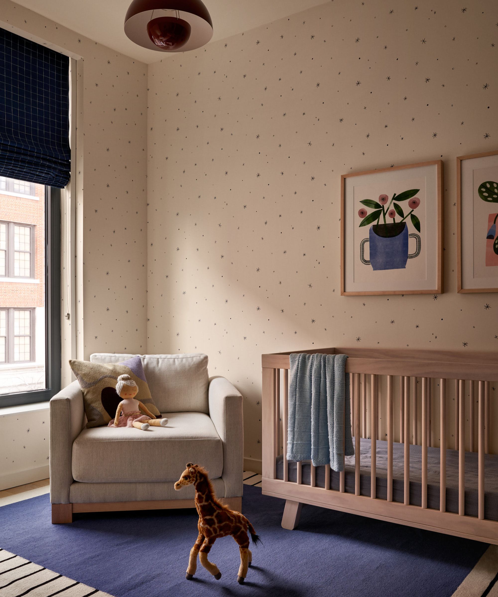 Nursery with wood cot, blue rug, armchair and polka dot wallpaper with two prints framed on wall