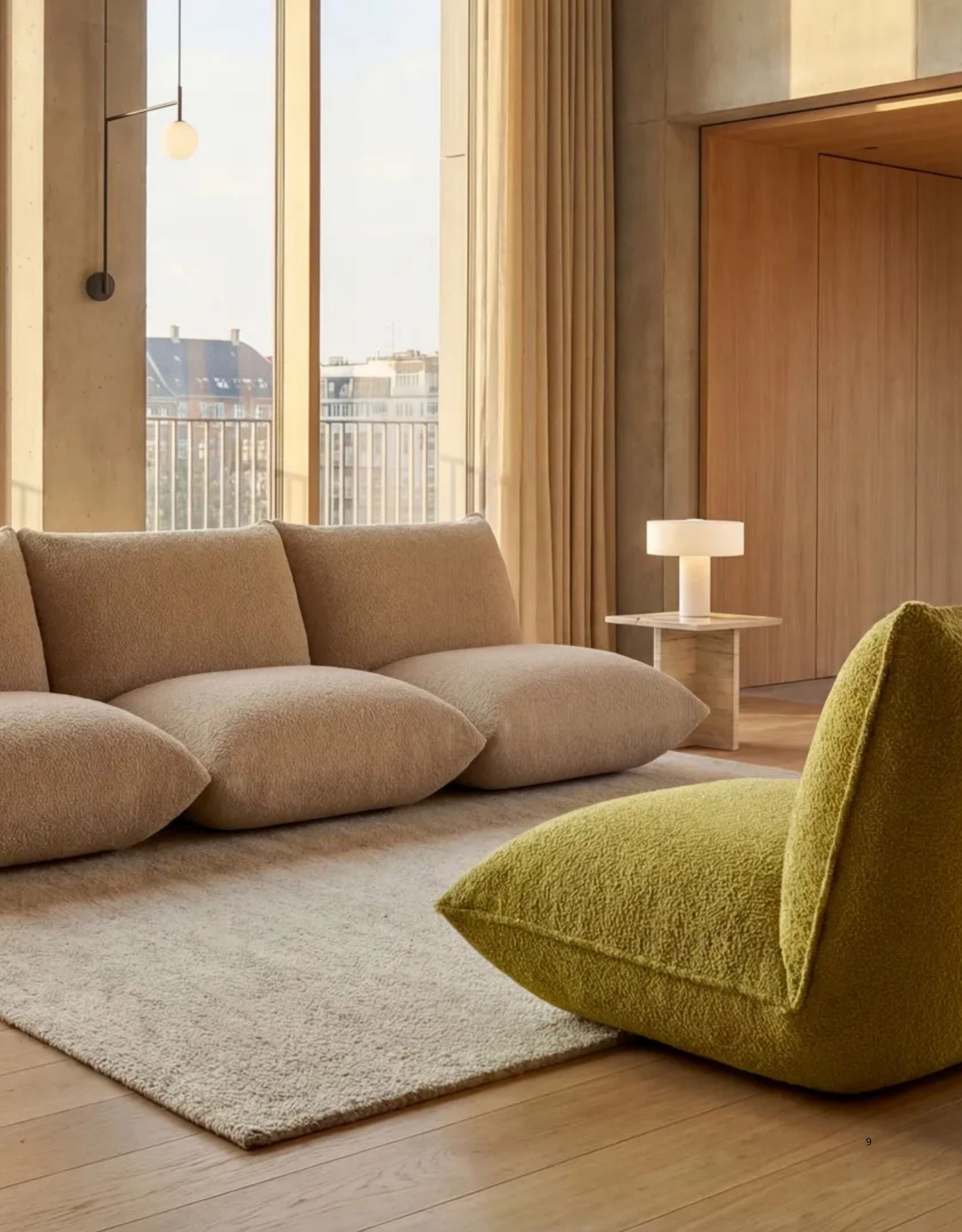 Image of a contemporary, luxury living room with high windows, wood floors, wood walls, and concrete walls. There is a white, armless sofa and a green accent chair.