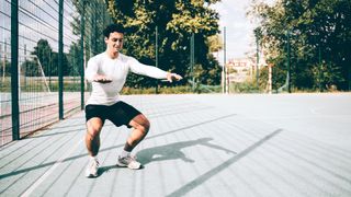 Male performing squat outside in a park
