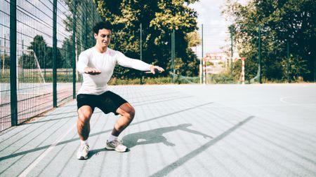 Male performing squat outside in a park