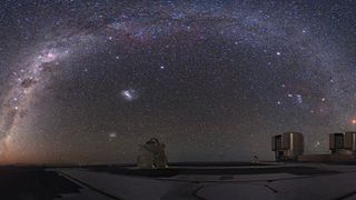 millions of stars glitter above several round buildings in a desert