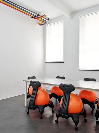 White conference room with exposed colourful piping and conference table with yoga ball chairs