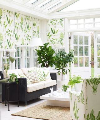 Light and bright white conservatory with black wicker sofa and green and white patterned curtains and armchair