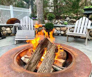 A rusty fire pit with two adironrack chairs in the background