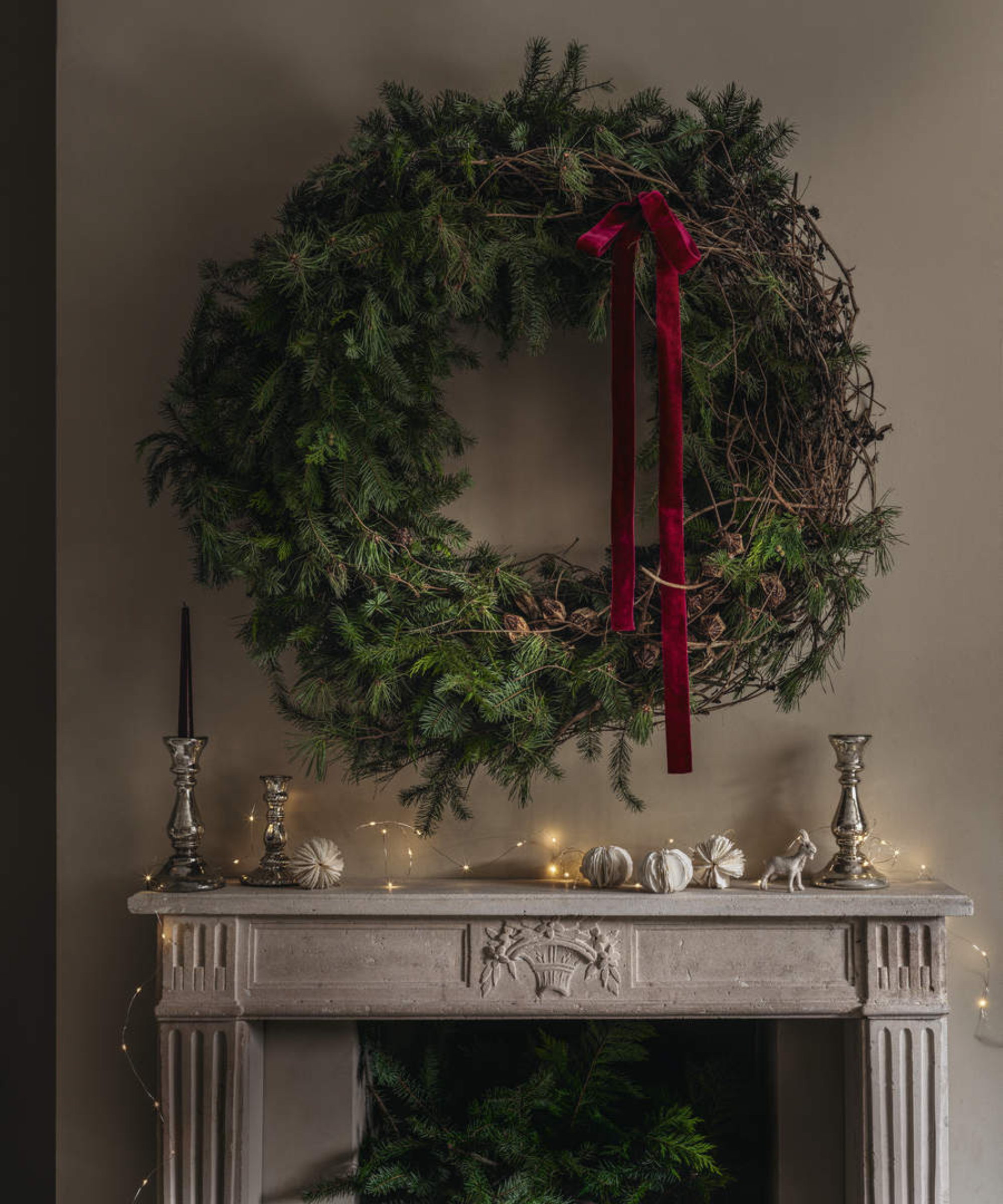 a large green wreath hanging over a stone mantel with candle holders on top of it