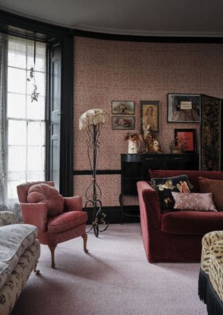 A living room with pink patterned wallpaper, a pink sofa and patterned chairs
