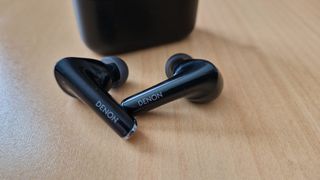 Denon Noise Cancelling Earbuds lying on a table next to their case