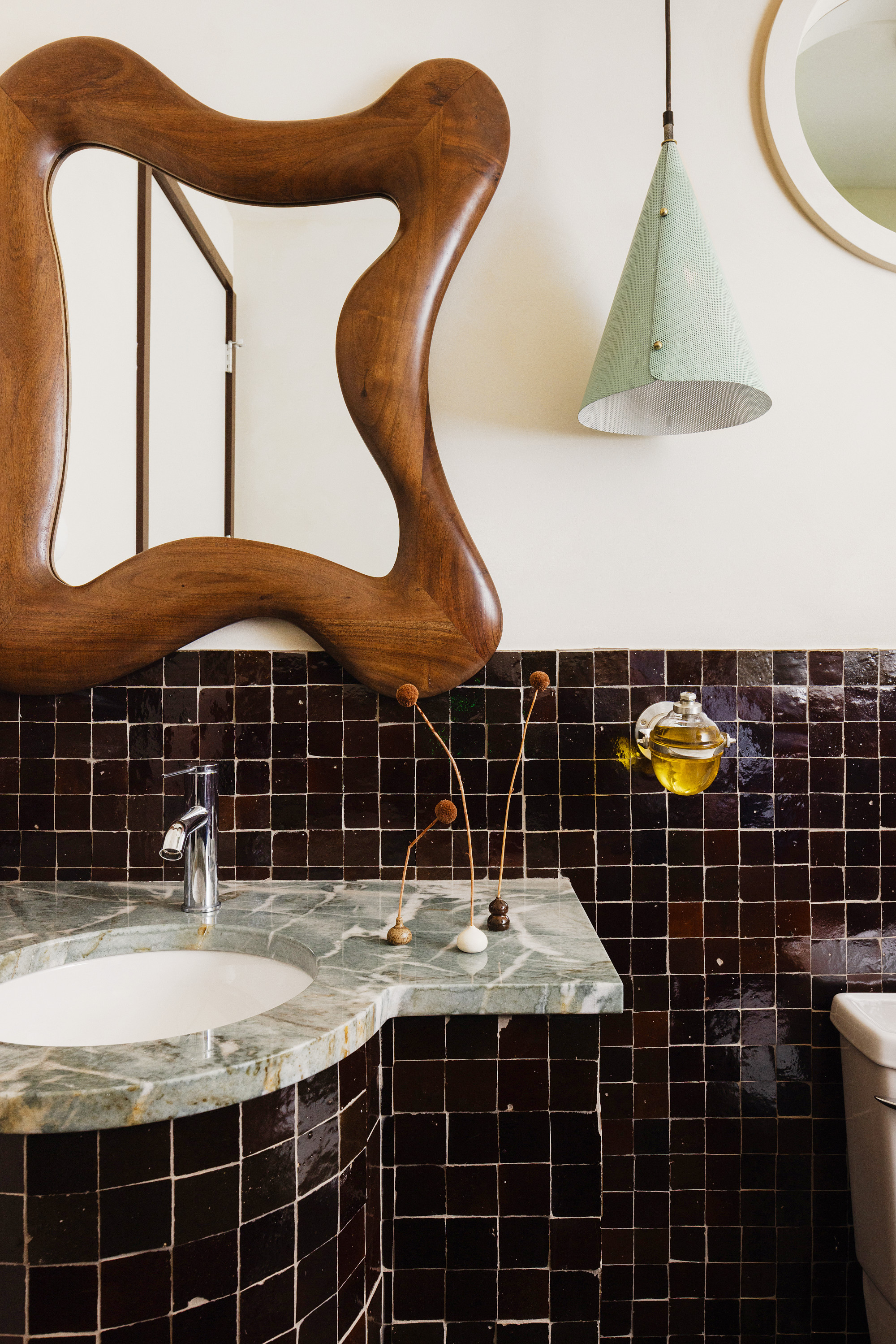 Powder room with dark brown zellige tiles, pale green stone countertop, pale green pendant and organic wood mirror