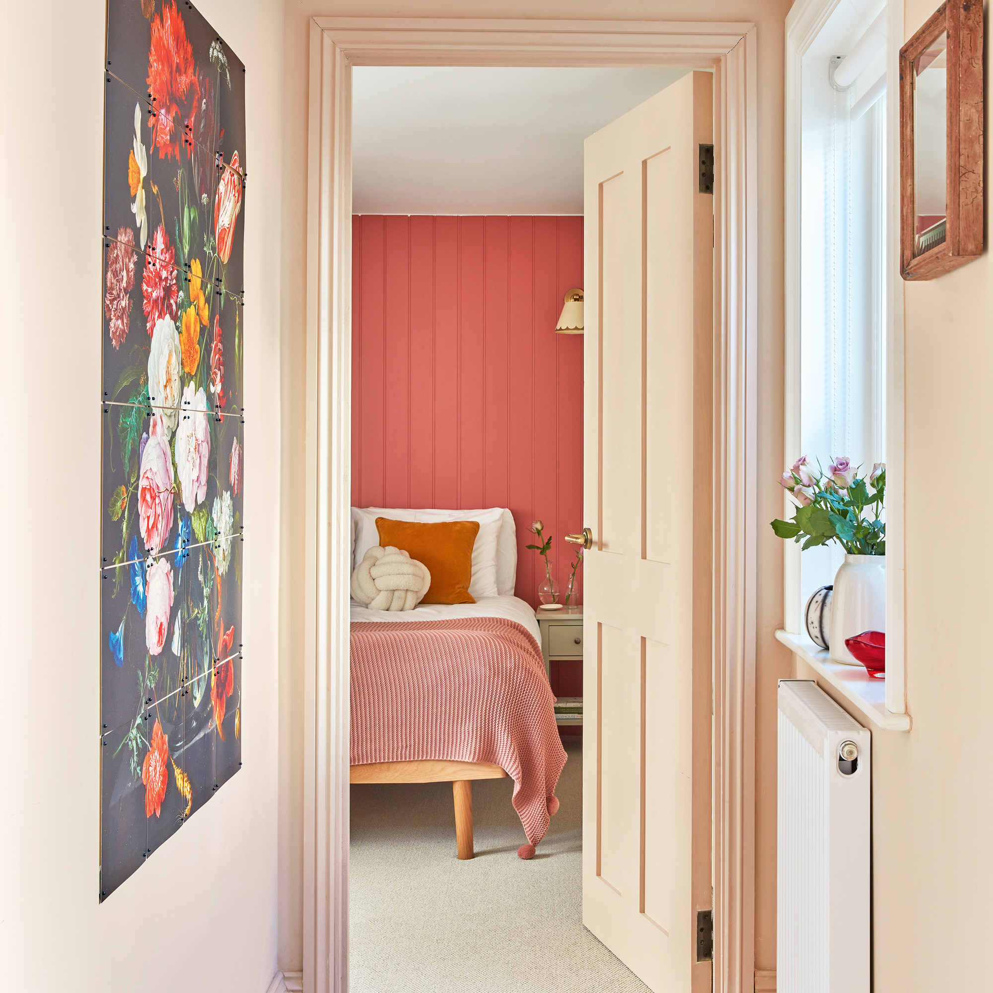 the view from a hallway with peach-painted walls into a small bedroom with bold pink painted panelled walls