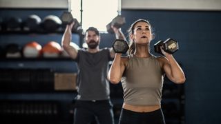 Two people working out with dumbbells in dark gym