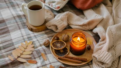 Cozy home at fall. Burning candle, mug coffee or tea, fall leaves on cozy bed. Knitting warm woolen sweater in the fall weekend