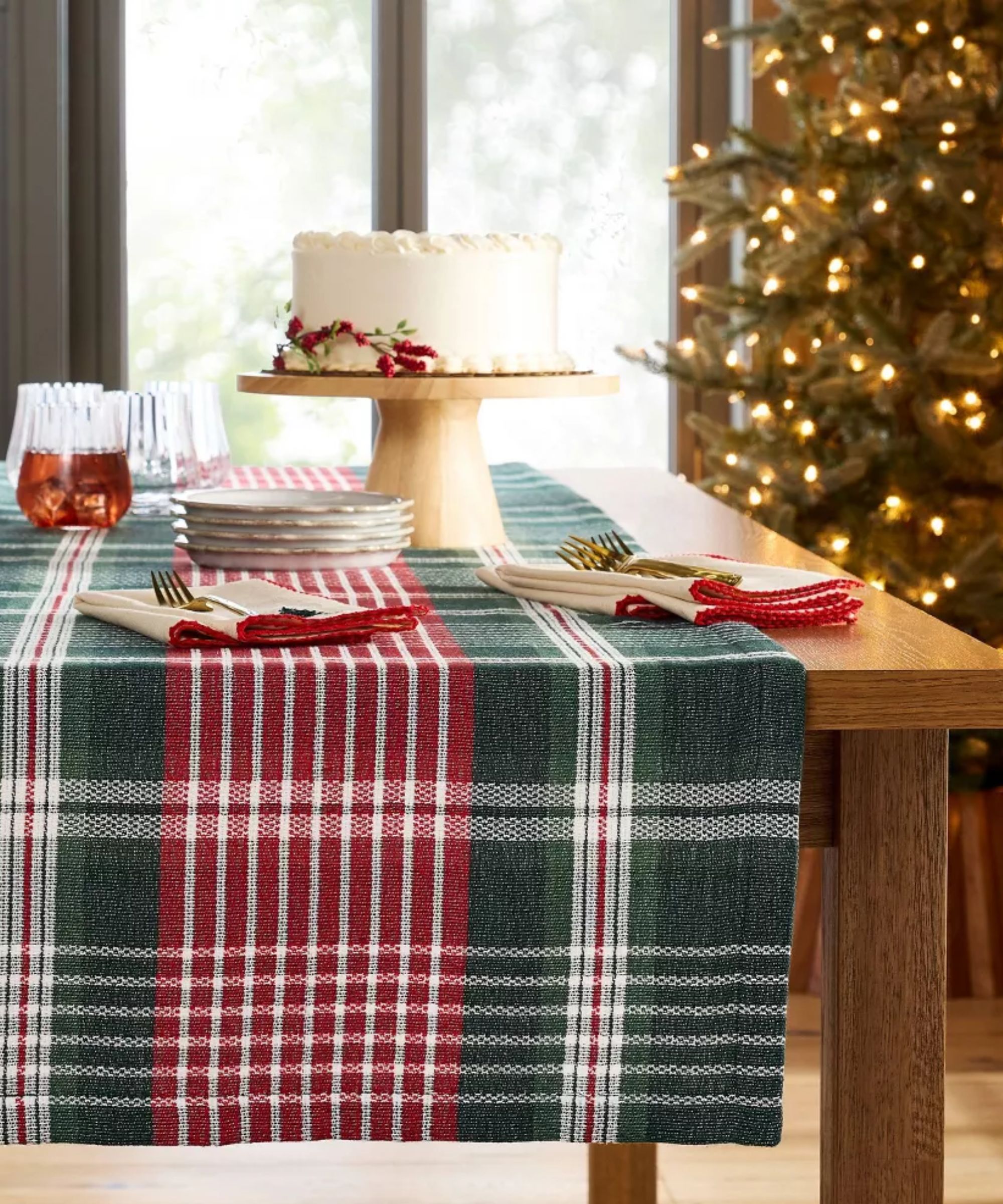 Table with plaid runner, Christmas napkins, fluted glasses and a wood cake stand