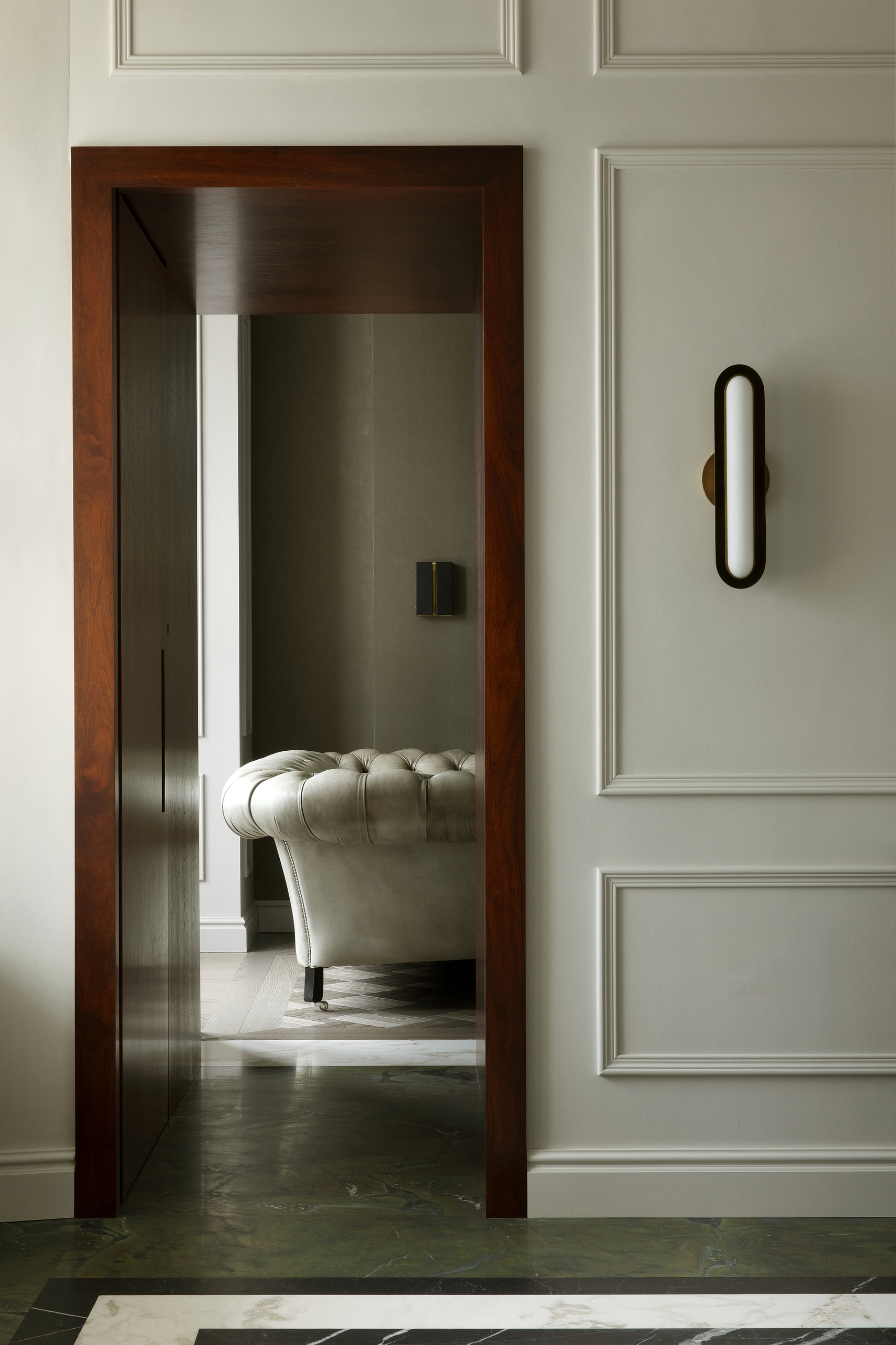 A wooden doorway on a white wall in a room that has emerald green flooring. You can see an off-white sofa through the doorway.