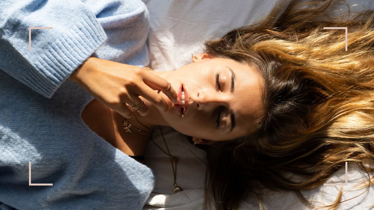 A woman lying on a bed with her hair sprad out behind her, to illustrate scalp oil for hair growth