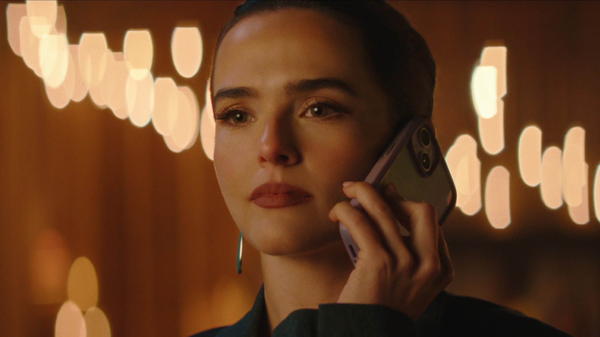 Zoey Deutch holding a phone up to her right ear.