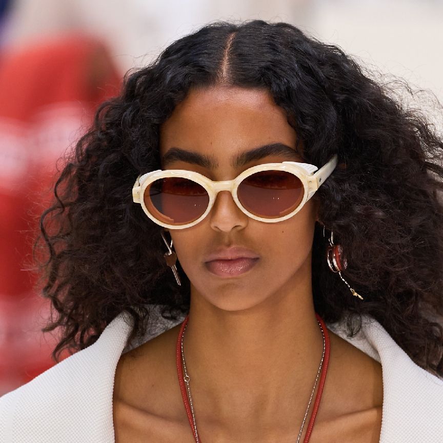 a woman with curly hair and bold brows wearing white sunglasses