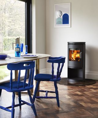 dining area with black freestanding log burner, cream table and blue wooden dining chairs