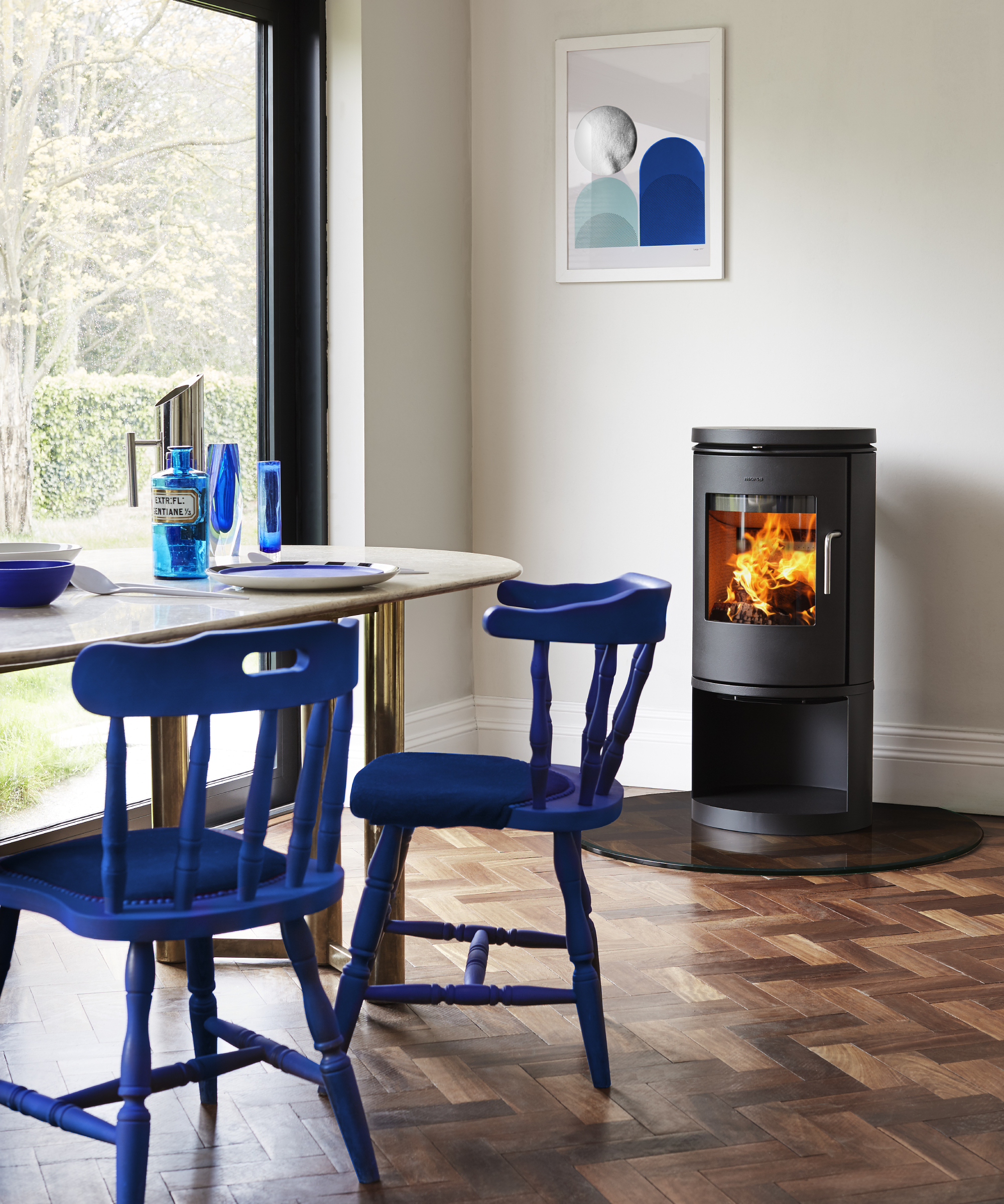 dining area with black freestanding log burner, cream table and blue wooden dining chairs