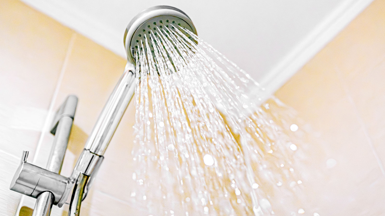 Shower on beige tiled wall with water pouring out