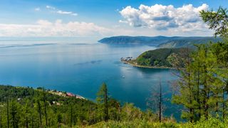 A picture of a large blue lake with a hilly, forested shoreline