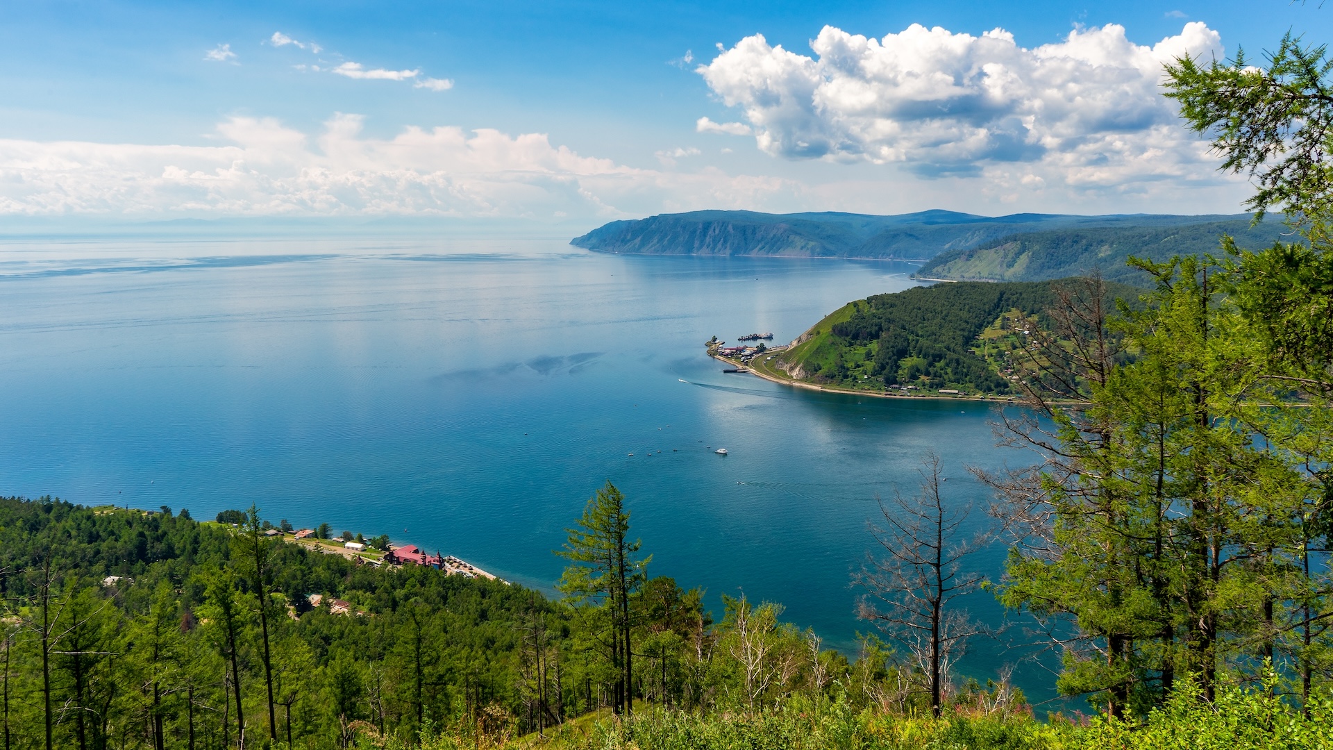 Gambar danau biru besar dengan garis pantai berbukit dan berhutan