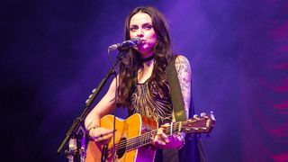 Amy McDonald performs live with her acoustic guitar, bathed in purple light