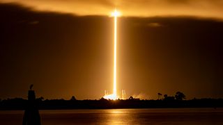 a long-distance, long-exposure photo shows a rocket launching atop a pillar of flame.