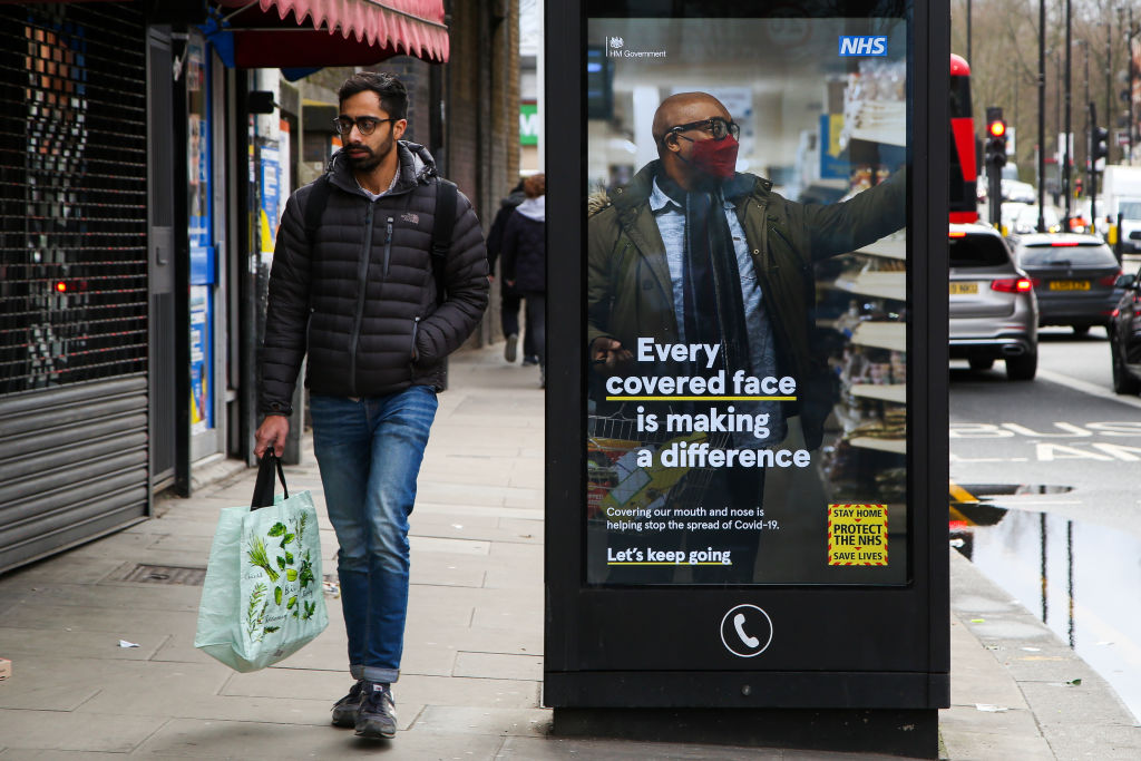 Man walks down the street next to 'wear a mask' sign as lockdown is working in the UK