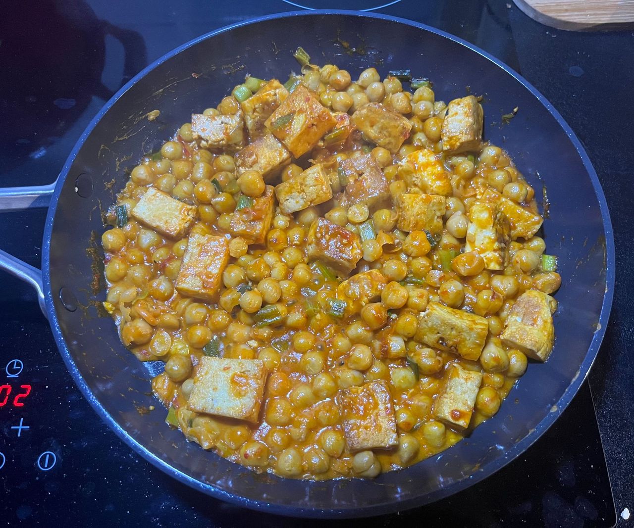 A black ceramic frying pan on a black stovetop with a chickpea tofu meal inside.