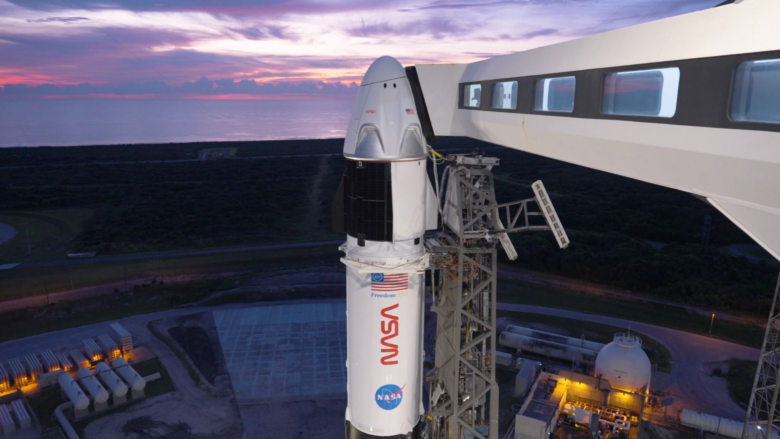 a white rocket and space capsule stand on a launch pad at dawn