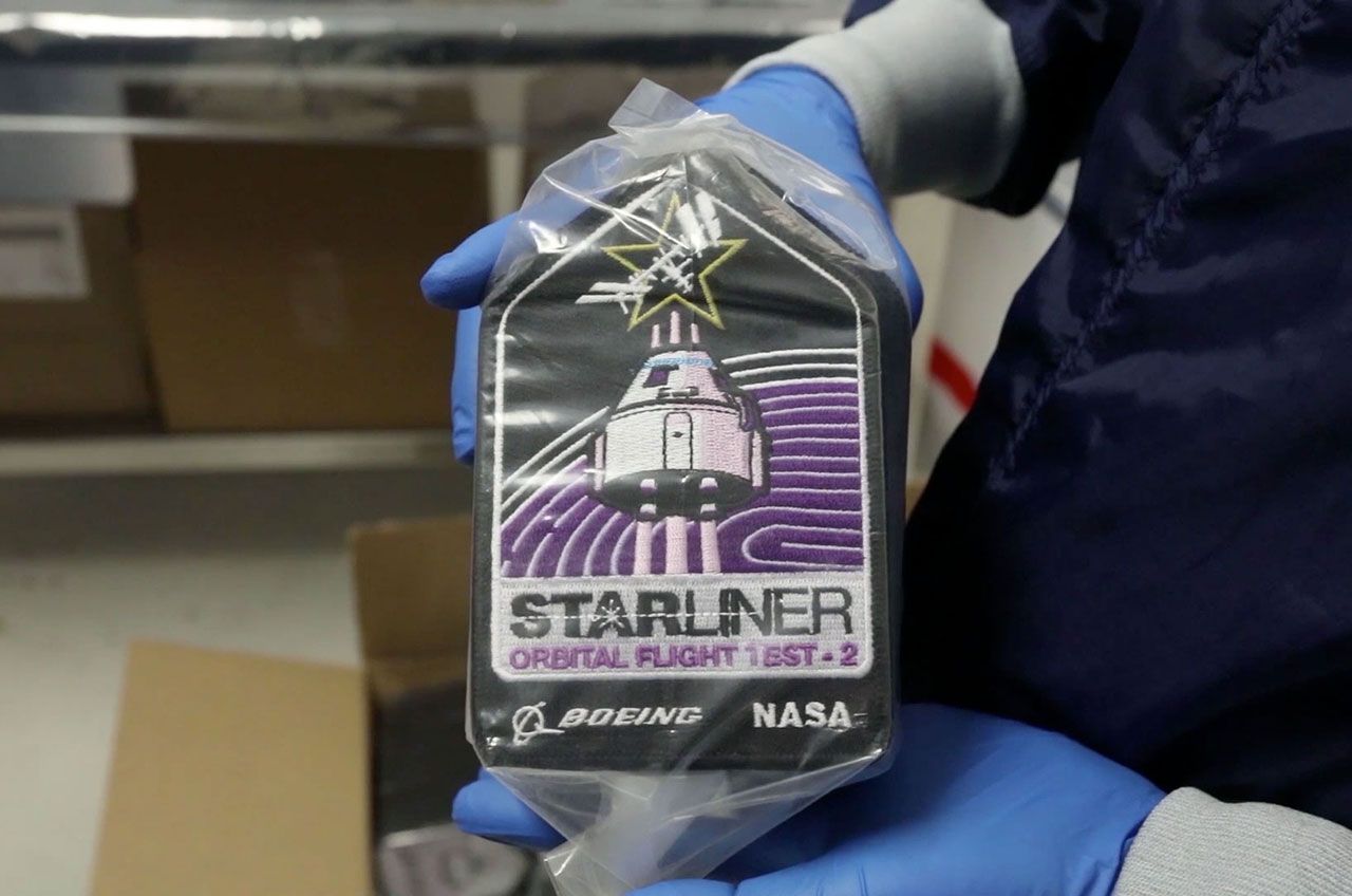 A Boeing technician holds a package of CST-100 Starliner Orbital Flight Test-2 patches to be flown on board the mission.