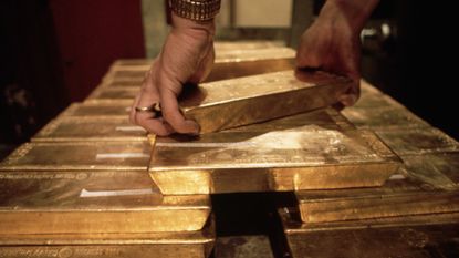 Male hands wearing a gold watch reach down to grab solid bars of gold