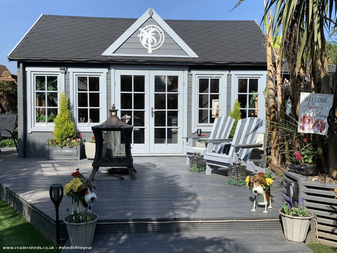A boat house turned into a shed with blue wooden doors and glass windows reflecting the furniture around such as chairs and tables and a firepit