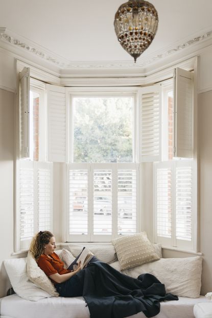 White wooden bay window with woman reading on seating space with cushions