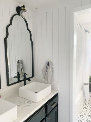 White guest bathroom with wall paneling and matching black rim mirrors