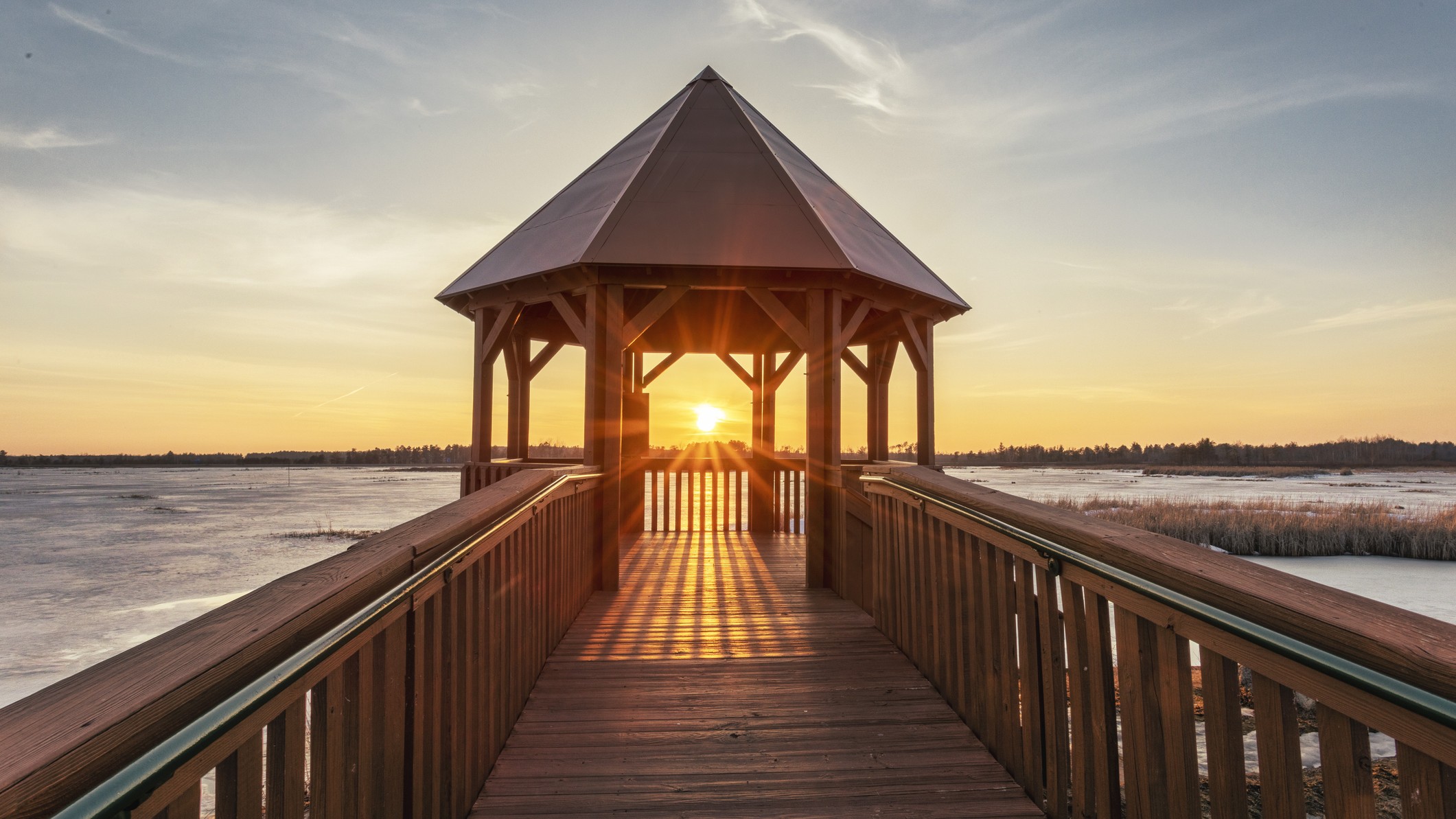 image of Houghton Lake Flats Gazebo Spring Equinox Sunset, Roscommon, Michigan. The sun appears in the center of the scene glowing golden.