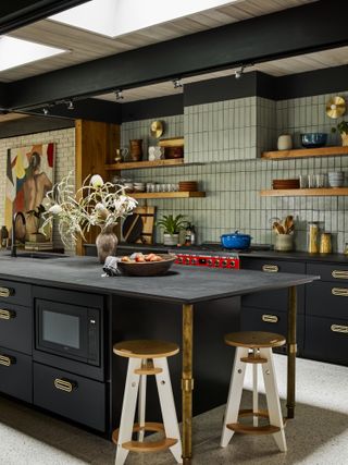 Black kitchen with textured island extended and supported by brass legs