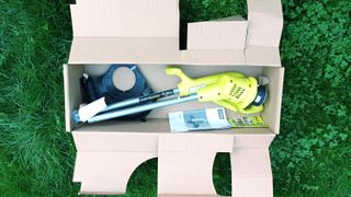 Ryobi 18V ONE+ Cordless Grass Trimmer in the box on grass background