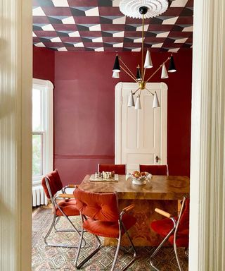 a dining room with crimson walls, white door and plush velvet dining chairs