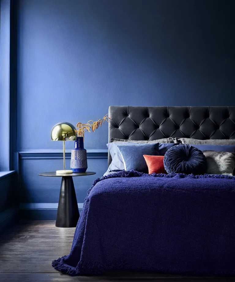 A dark blue bedroom featuring a bed with a blue velvet headboard